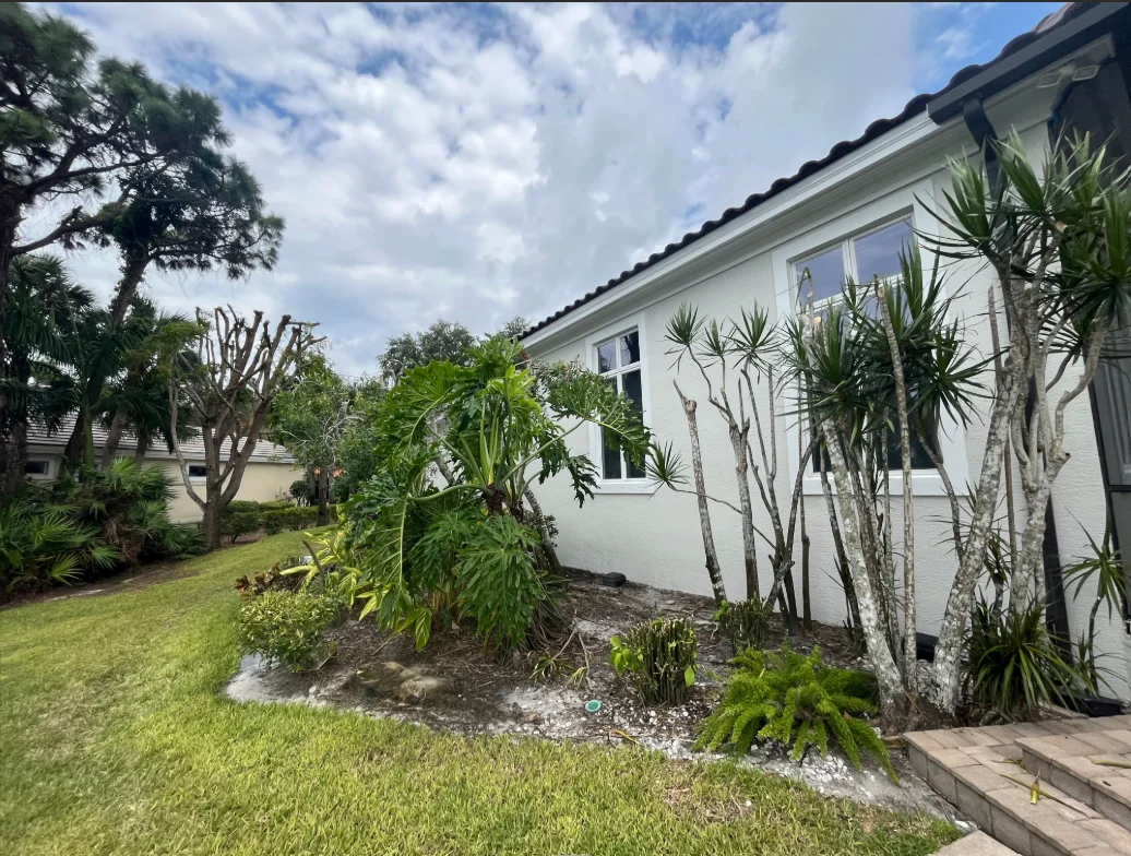 White painted residential home with tropical landscaping and dark roof trim in Naples