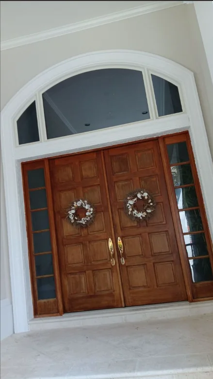 Stained wood double doors with white trim and arched transom window in Naples home