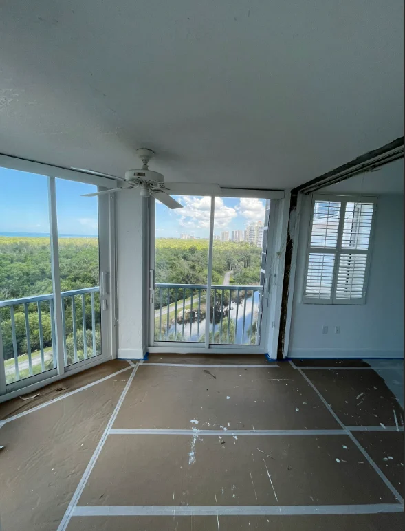 High-rise condo interior with fresh paint prep, protective coverings, and waterfront views through glass doors