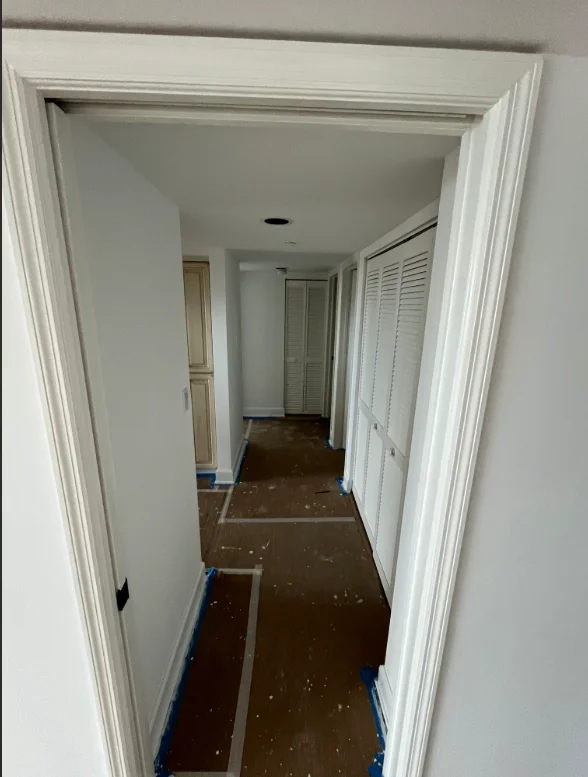 White-trimmed hallway with freshly painted walls and protective blue tape along floor
