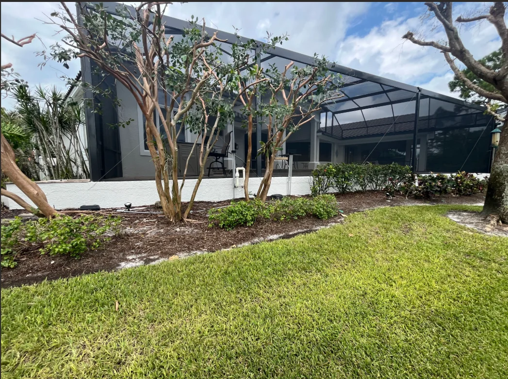 Modern home with white and dark gray exterior paint, black metal lanai cover, and landscaped yard