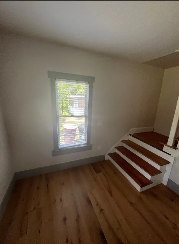 Painted stairwell with white trim, hardwood floors, and window with shutters
