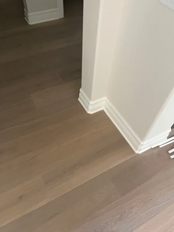 White baseboard trim and corner molding installed along interior walls with hardwood flooring