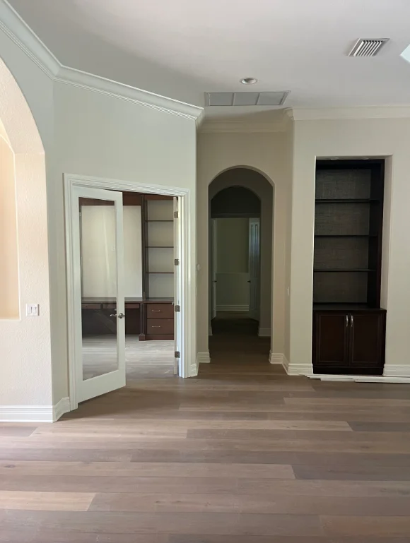Interior room with neutral painted walls, white trim, arched doorway, and dark wood built-in shelving