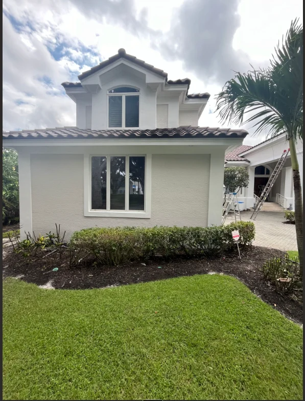 White two-story home with fresh exterior paint, dark roof, and landscaped front yard in Naples