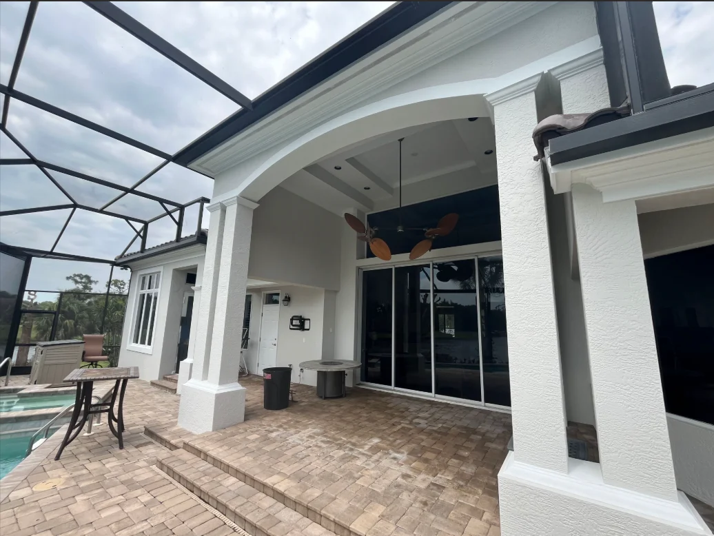 White painted modern home exterior with arched entryway, columns, and brick patio