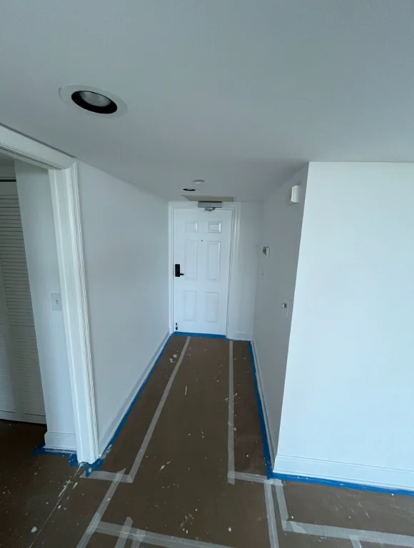 White painted hallway with recessed lighting and blue floor protection tape